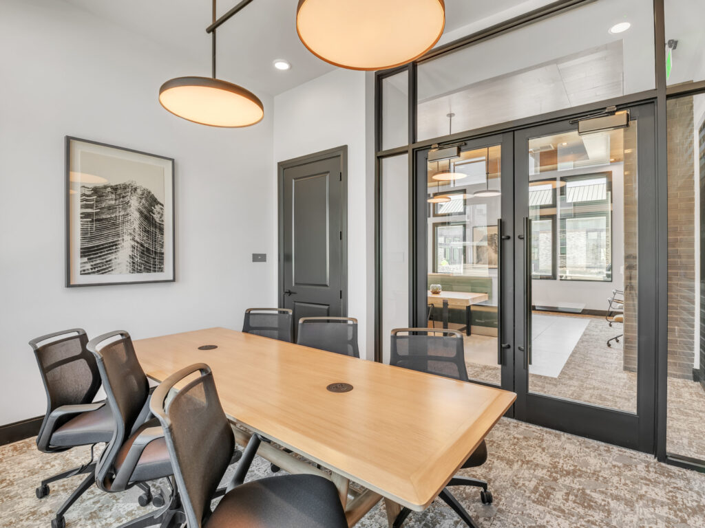 Modern conference room with wooden table, six chairs, large windows, and abstract wall art.