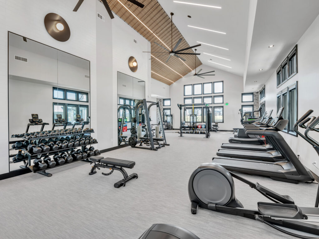 Spacious fitness center with treadmills, weight rack, exercise bikes, and high ceilings with large windows.