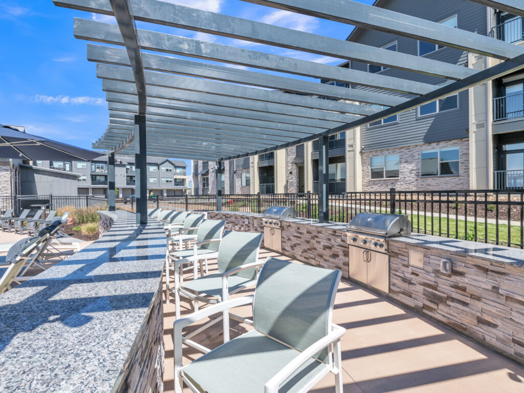 Outdoor apartment grill area with chairs, pergola, and modern buildings in background
