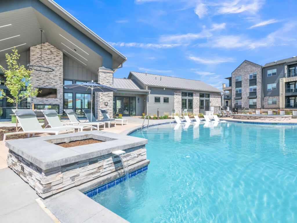 Outdoor swimming pool with sun loungers, umbrellas, and modern building backdrop
