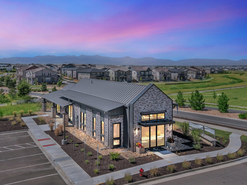 Modern building with large windows, surrounded by landscaped area and residential neighborhood at dusk.