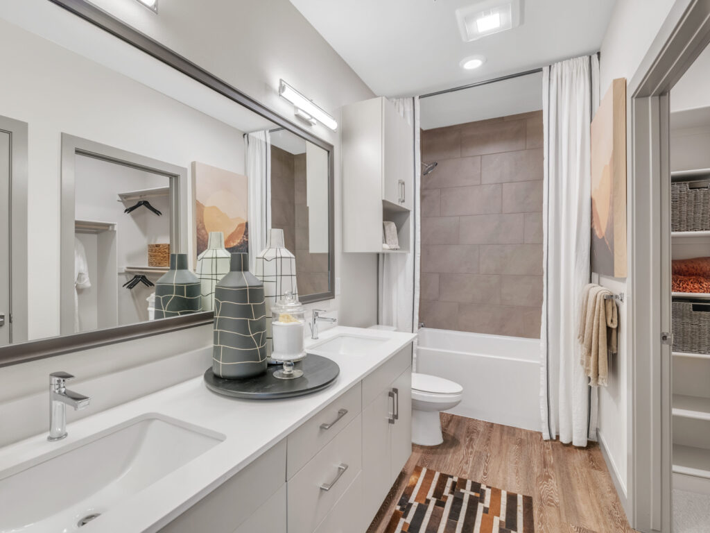 Modern bathroom with double vanity, decorative vases, large mirror, bathtub, and open shelving.