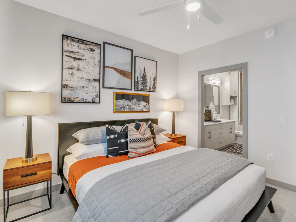 Modern bedroom with gray and orange bedding, wall art, and en-suite bathroom.