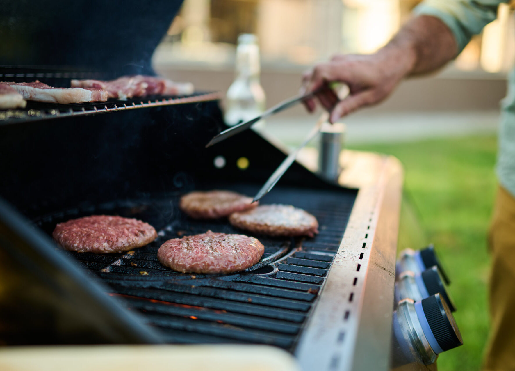 Grilling hamburgers on an outdoor barbecue with a hand holding tongs