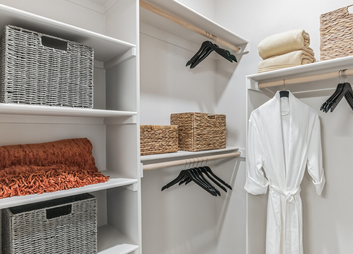Organized closet with shelves holding baskets, hangers, a robe, folded towels, and an orange blanket.