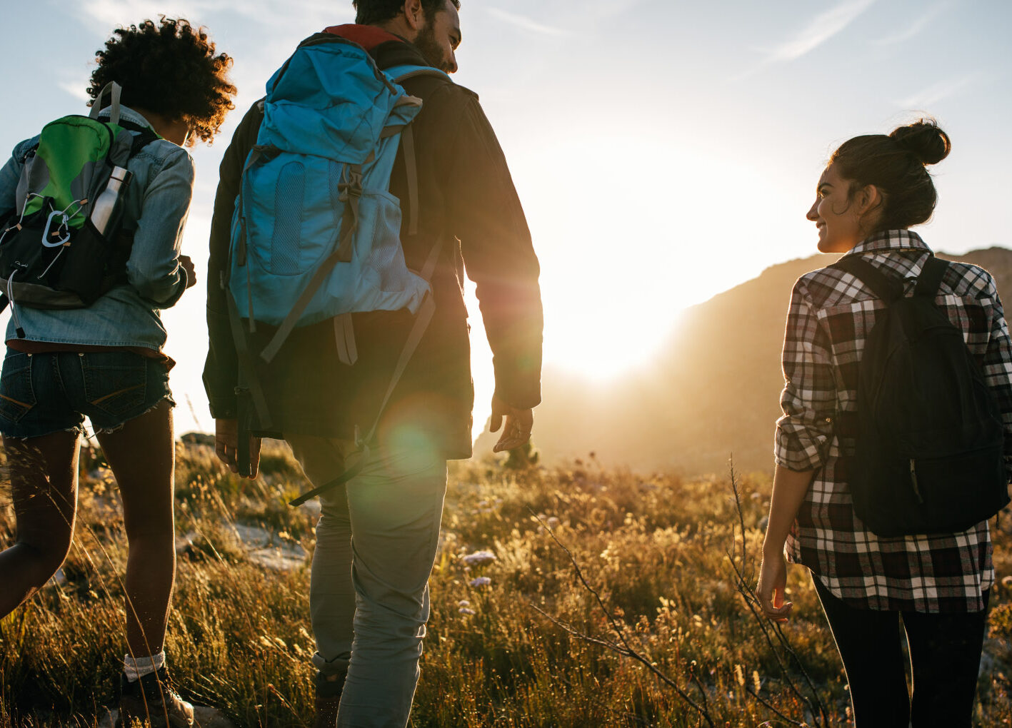 Three people hiking at sunset with backpacks, smiling and enjoying the scenic view.
