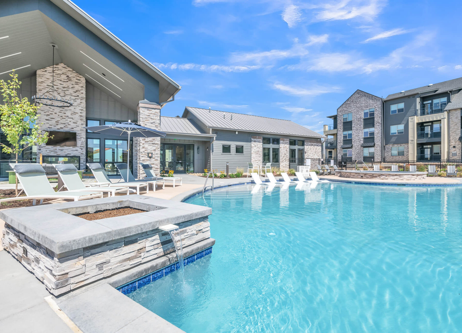 Luxurious outdoor pool area with sun loungers, umbrellas, and modern buildings under a clear blue sky