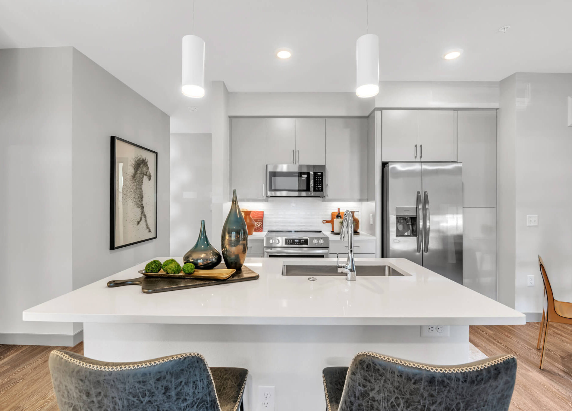 Modern kitchen with sleek appliances, decorative vases on a white island, and horse art on the wall.